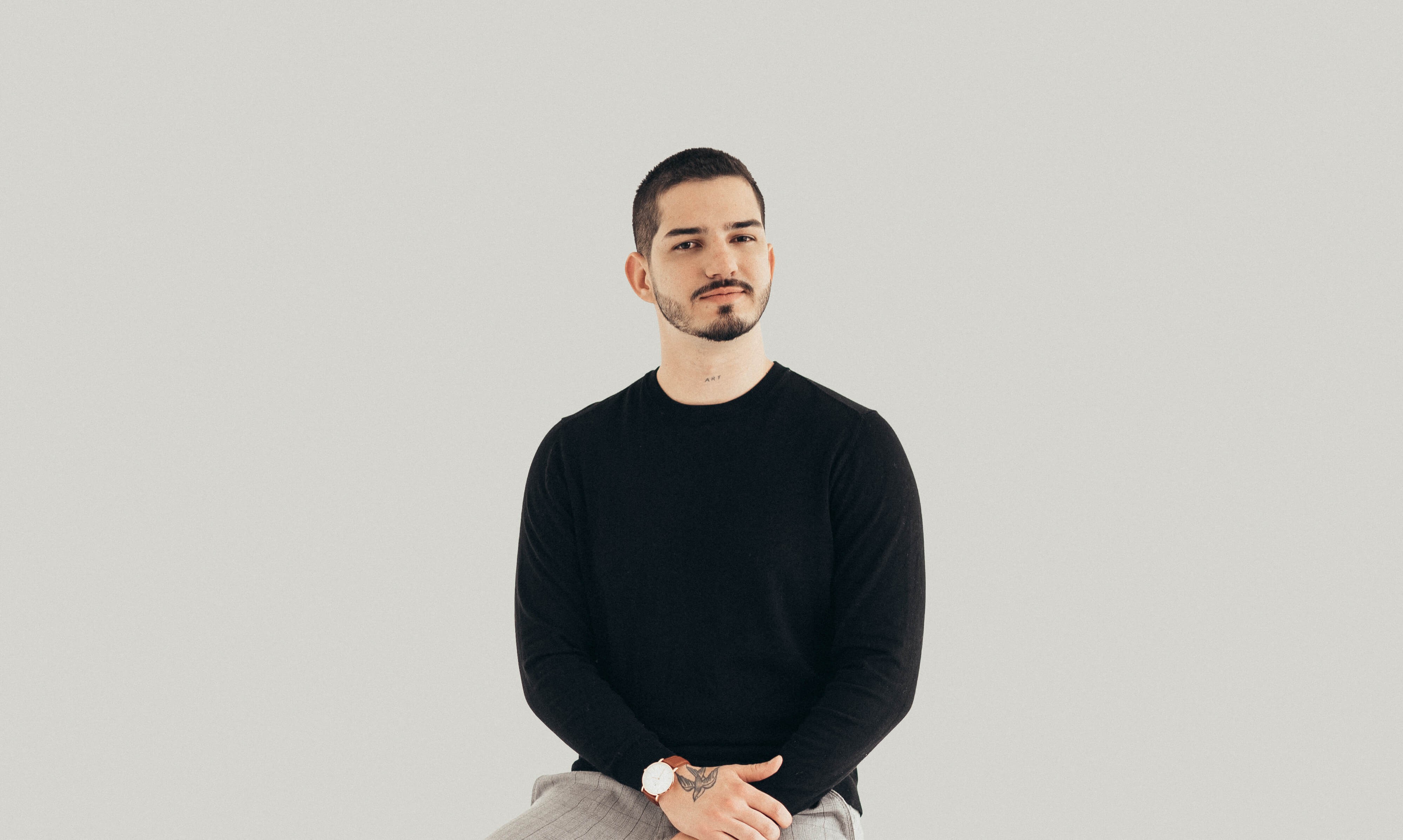 Man with short hair and beard in a black sweater sitting against a plain background.