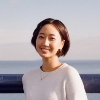 Smiling woman with short brown hair and white sweater standing outdoors near water.